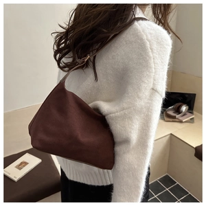 Detail of a dark brown vintage matte underarm bag worn over a white knitted sweater