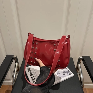 Red patent leather crossbody bag with silver rivet studs on a sleek minimal chair