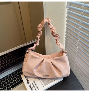 Detailed view of pink pleated handbag with metallic logo resting on a laptop desk