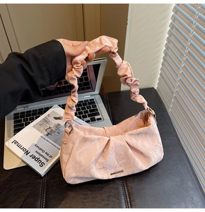 Detail of pink ruched shoulder bag with gold metal logo on a modern desk with soft light