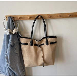 Detail of camel suede tote bag with black decorative straps hanging on a wooden hook