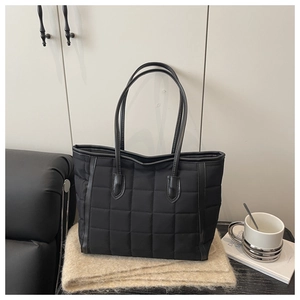 Detail of black quilted tote bag with square pattern texture and leather shoulder strap