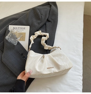 Detailed macro view of cream pleated shoulder bag featuring elegant metal logo plate