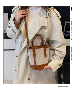 Detail of canvas bucket bag with brown leather trim and slim shoulder strap on model