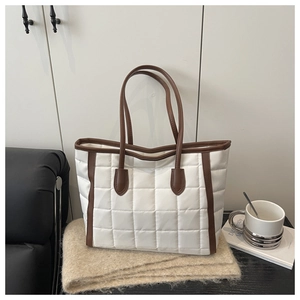 Detail of white quilted tote bag with brown leather trim and long shoulder handles