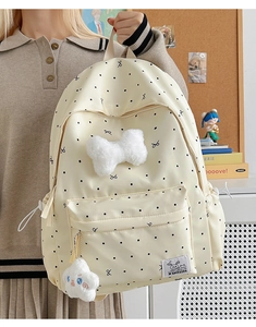 Close-up of cream polka dot backpack featuring plush bow and cloud keychain detail