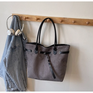 Detail of grey suede tote bag with black leather straps and metal eyelet accents