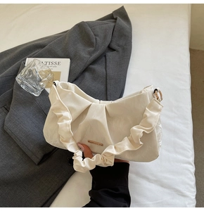 Detail of a creamy white pleated cloud bag featuring golden rings and metallic logo