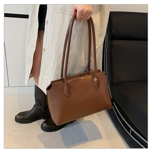 Detail of a brown leather tote bag featuring thin shoulder straps and wave-cut top edges