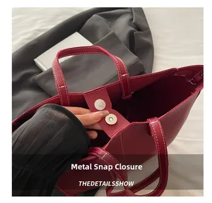 Detail of red faux leather tote bag showing polished magnetic closure and white stitching