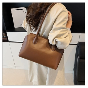 Close-up of minimalist brown leather tote bag showing smooth matte texture and shoulder strap