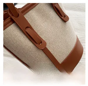 Detailed close-up of brown leather stitching and beige woven fabric on a bucket bag