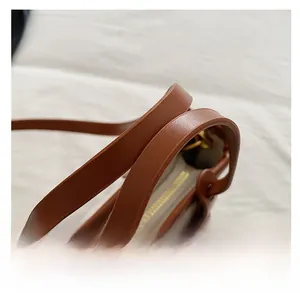 Detail of durable brown leather handle and gold zipper on cream canvas bucket bag