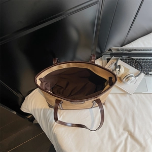 Grand sac cabas bicolore kaki et marron avec ordinateur et accessoires sur un lit blanc