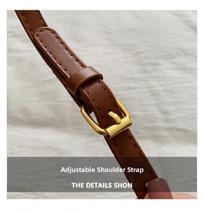 Detail of brown leather adjustable shoulder strap with gold buckle on white fabric