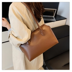 Close-up of a brown leather tote bag worn as a shoulder bag in an office setting