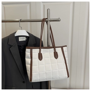 Detailed view of white quilted tote bag with brown handles hanging on a metal rack