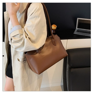 Brown tote bag on shoulder showing large capacity and smooth texture in a modern office