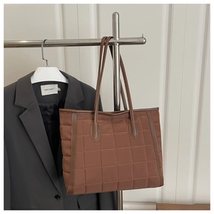 Detail view of brown quilted tote bag with diamond stitching on a metal hanger