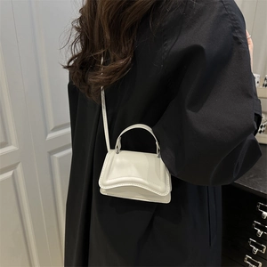 Minimalist white PU leather crossbody bag with curved flap shown on model outfit