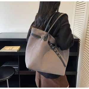 Detail shot of a large grey suede tote bag with black leather straps and metal eyelet belt