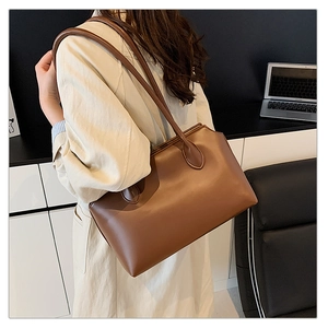 Brown leather tote bag shown on model shoulder in a minimalist office setting