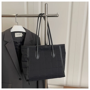 Detail of black quilted tote bag with satin finish and leather straps on hanger