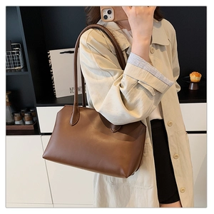 Close-up of a minimalist brown leather tote bag held by a model in a home setting