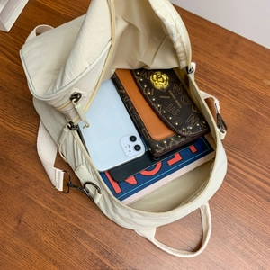 Large capacity cream nylon backpack showing spacious interior with wallet and phone