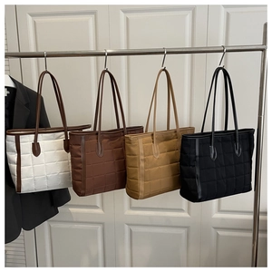 Detailed view of four quilted tote bags in white, brown, khaki and black displayed on a rack