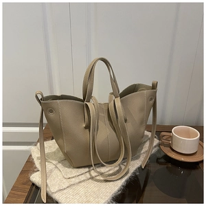 French design beige leather bucket bag on knit sweater next to a coffee cup