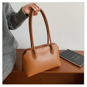 Detail of a brown leather tote bag with slim shoulder straps held by a model