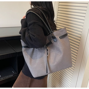 Detail of grey suede tote bag with black leather straps worn by model in a modern room