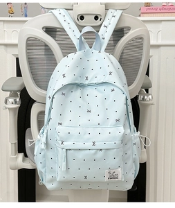 Light blue polka dot backpack with bow pattern and front pocket shown on a chair