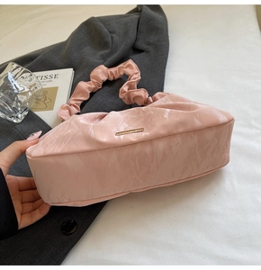 Detail of light pink pleated cloud bag with golden metal plaque on grey suit background