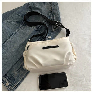 Detail view of white nylon crossbody bag with adjustable strap and zip closure on denim