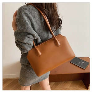 Detail view of large brown faux leather tote bag with slim shoulder straps on a model