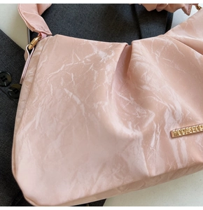 Detail of pink pleated underarm bag with gold logo on dark grey suit background