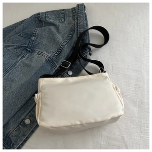 Overhead view of off-white nylon crossbody bag with wide black strap and side pleats