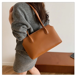 Side view of a large brown leather tote bag worn by a model in a minimalist room