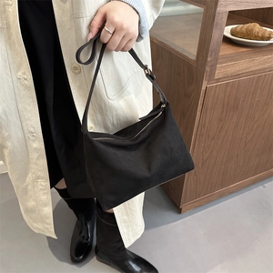 Minimalist black suede shoulder bag with gold hardware shown on a trench coat model