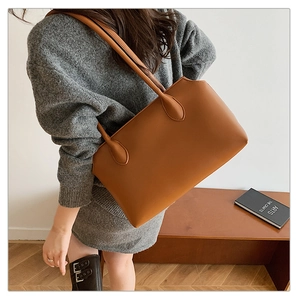 Brown leather tote bag worn by a model, showcasing large capacity and minimalist style