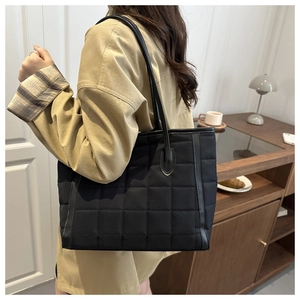 Detail of black quilted tote bag with padded texture and leather shoulder straps for daily use