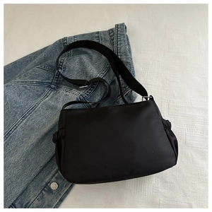 Flat lay of black nylon crossbody bag with wide strap on denim and fabric background