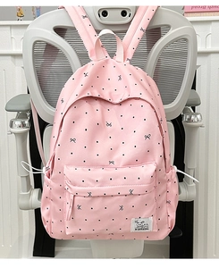 Close-up of pink polka dot backpack with a bow detail hanging on a gray chair
