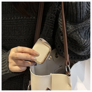 Mini cream-white pebble leather coin purse with gold clasp being put into a large tote