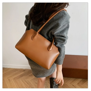 Brown tote bag with teardrop handle detail shown on shoulder in a minimalist room