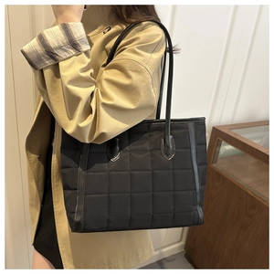 Detailed view of black quilted tote bag with large square stitching and thin handles