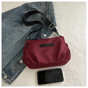 Detail of burgundy oxford cloth crossbody bag with adjustable strap and brand logo