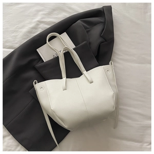 Detail of white litchi-grain leather tote bag with side drawstring on black blazer